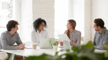 Multiracial male and female colleagues discussing document at team meeting or corporate office briefing, diverse friedly african and caucasian partners talking about contract at group negotiations